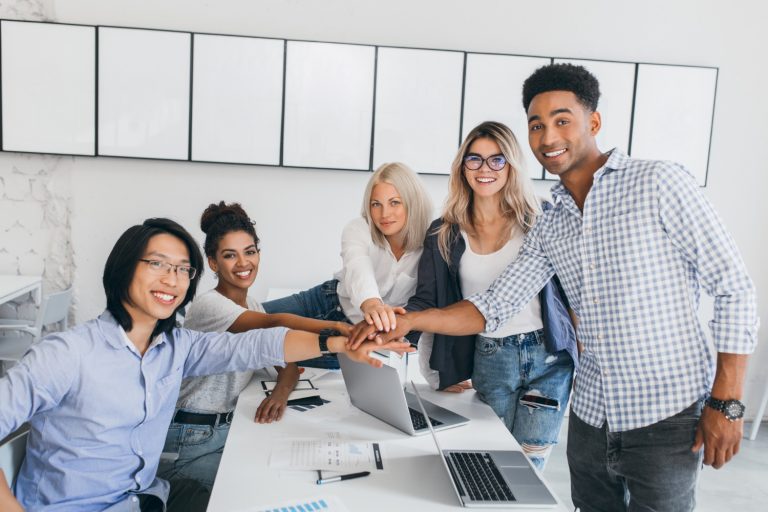 portrait-asian-young-man-his-african-friend-posing-beside-table-with-laptops-documents-it-web-designer-shaking-hands-with-new-employee-office